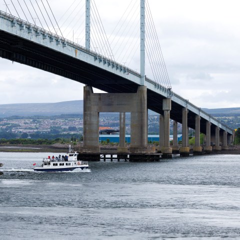 Boat passing under a large suspension bridge on a cloudy day.