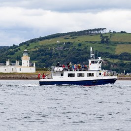 Boat sailing near lighthouse with green hills in the background.
